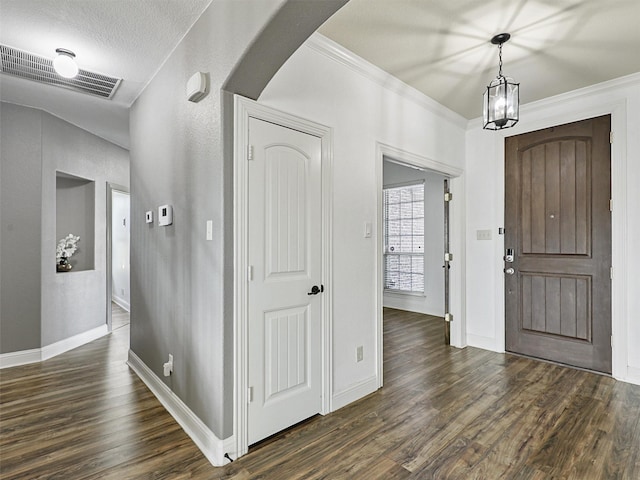 entrance foyer featuring dark hardwood / wood-style flooring, an inviting chandelier, ornamental molding, and a textured ceiling