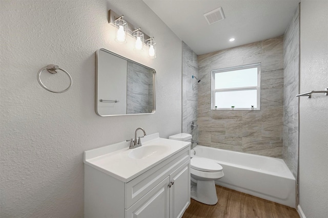 full bathroom featuring wood-type flooring, tiled shower / bath combo, vanity, and toilet