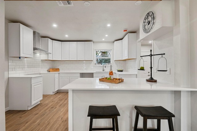 kitchen featuring kitchen peninsula, white cabinetry, light hardwood / wood-style flooring, and wall chimney exhaust hood