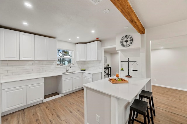 kitchen with white cabinetry, light hardwood / wood-style floors, sink, beam ceiling, and a breakfast bar area