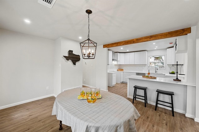 dining room featuring light hardwood / wood-style floors, sink, beam ceiling, and a chandelier