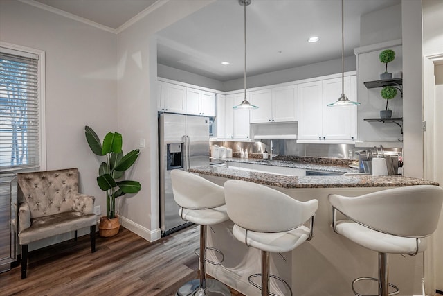 kitchen with crown molding, kitchen peninsula, stainless steel fridge, white cabinets, and decorative light fixtures