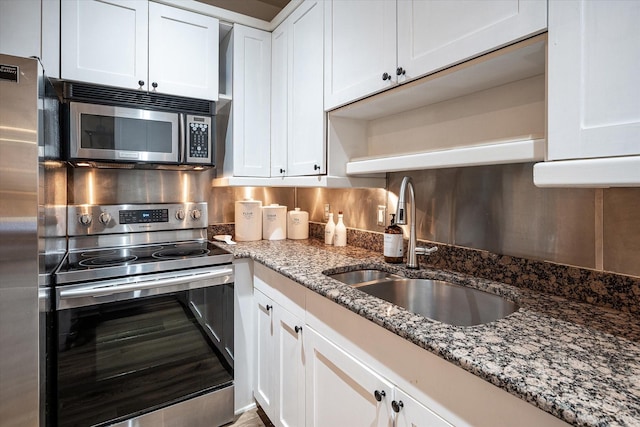 kitchen with stainless steel appliances, stone counters, sink, white cabinetry, and backsplash