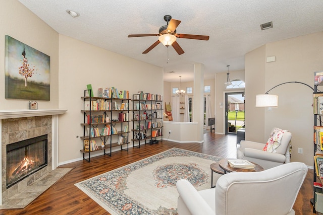 living room featuring a textured ceiling, ceiling fan, dark hardwood / wood-style floors, and a tile fireplace