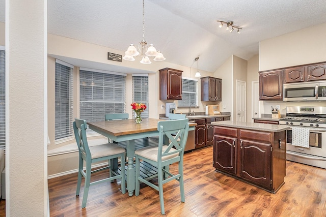 kitchen featuring decorative light fixtures, appliances with stainless steel finishes, a center island, and dark brown cabinets