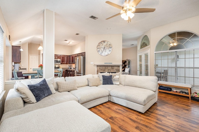 living room featuring a textured ceiling, ceiling fan, dark hardwood / wood-style flooring, and a stone fireplace