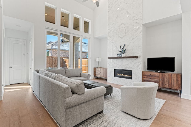 living room featuring a high ceiling, a premium fireplace, ceiling fan, and light hardwood / wood-style flooring