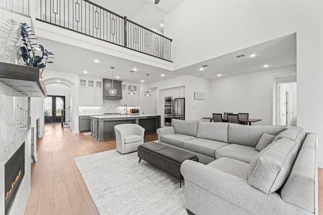 living room with a high ceiling, french doors, light hardwood / wood-style flooring, and a stone fireplace