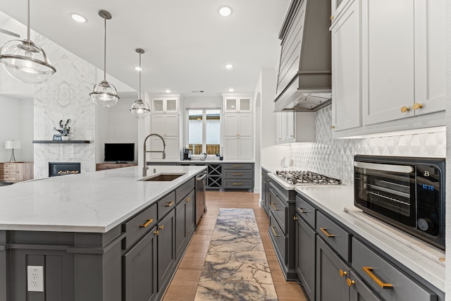 kitchen featuring tasteful backsplash, white cabinetry, a large island with sink, a tiled fireplace, and sink