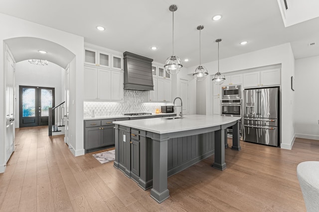 kitchen with custom exhaust hood, gray cabinetry, stainless steel appliances, an island with sink, and sink