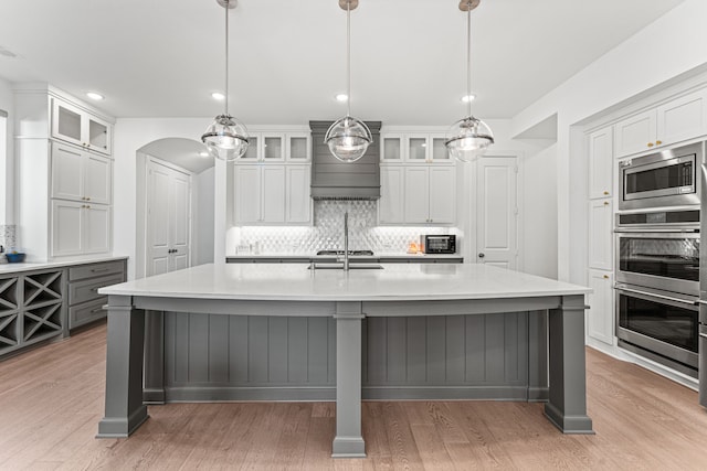 kitchen featuring a large island with sink, stainless steel appliances, white cabinets, and tasteful backsplash