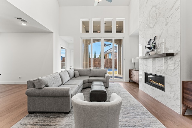 living room featuring a towering ceiling, a fireplace, ceiling fan, and wood-type flooring