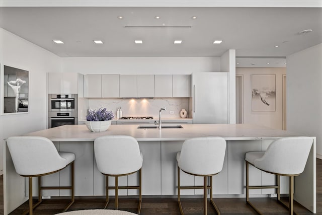 kitchen with stainless steel appliances, a breakfast bar, backsplash, white cabinets, and sink