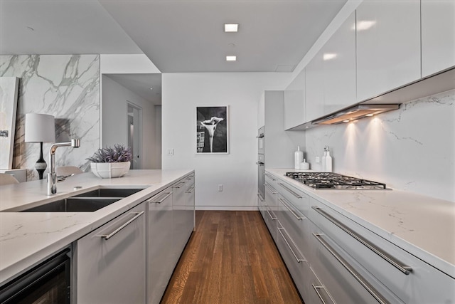 kitchen with light stone countertops, dark hardwood / wood-style floors, stainless steel gas stovetop, white cabinets, and sink