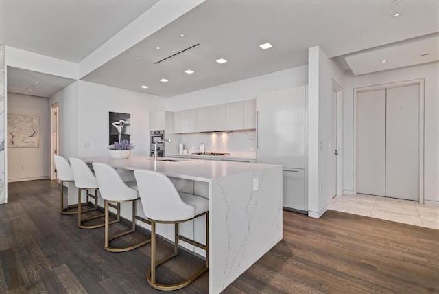 kitchen featuring hardwood / wood-style floors, a large island, stainless steel gas cooktop, white cabinetry, and sink