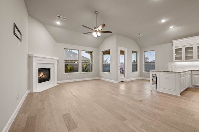 unfurnished living room with lofted ceiling, ceiling fan, light hardwood / wood-style flooring, and a healthy amount of sunlight