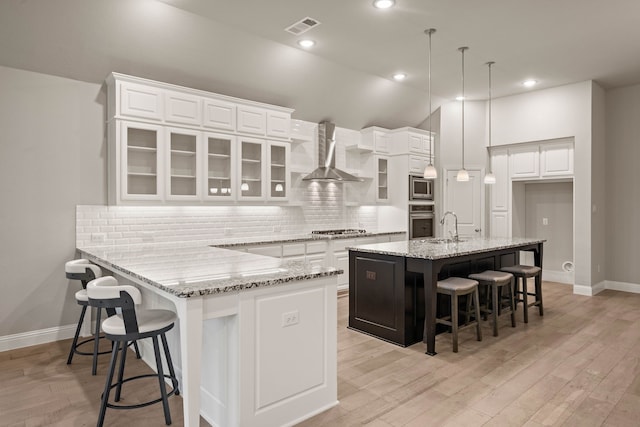 kitchen featuring white cabinets, a kitchen breakfast bar, hanging light fixtures, a center island with sink, and wall chimney exhaust hood