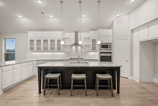 kitchen with wall chimney exhaust hood, white cabinetry, appliances with stainless steel finishes, a kitchen breakfast bar, and light stone countertops