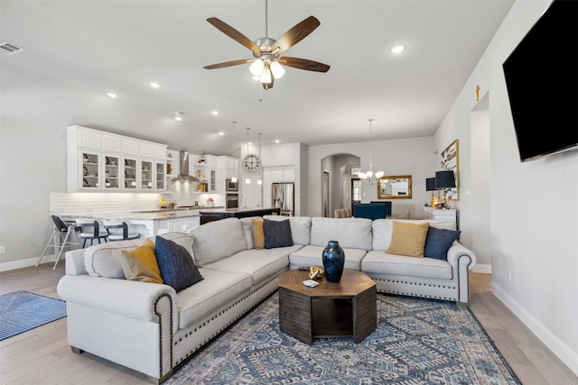 living room featuring ceiling fan with notable chandelier and light wood-type flooring