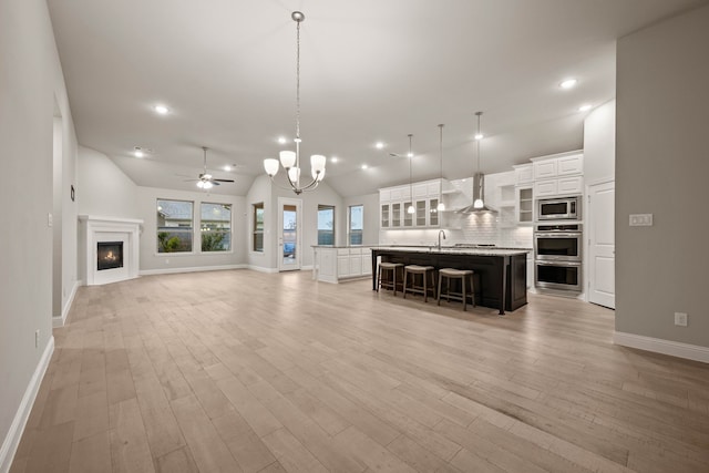 unfurnished living room featuring vaulted ceiling, sink, ceiling fan with notable chandelier, and light wood-type flooring