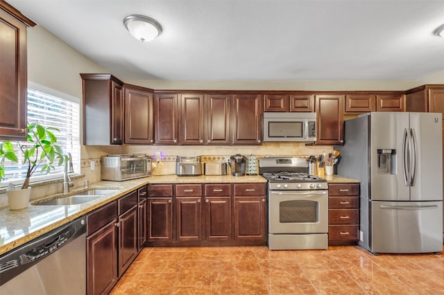 kitchen with light stone countertops, appliances with stainless steel finishes, tasteful backsplash, and sink