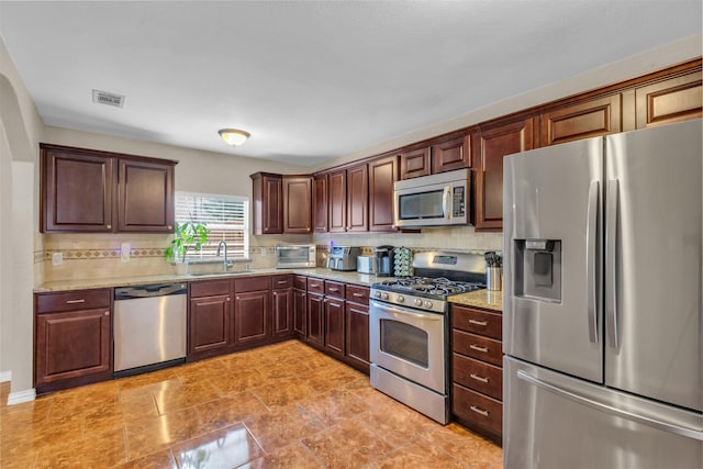 kitchen featuring light stone counters, stainless steel appliances, sink, and decorative backsplash