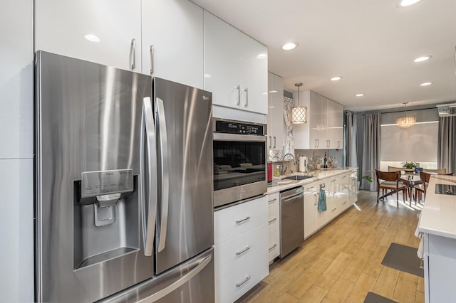 kitchen with pendant lighting, light wood-type flooring, white cabinets, appliances with stainless steel finishes, and sink