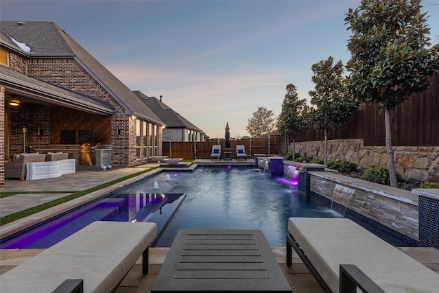 pool at dusk with a patio, pool water feature, and area for grilling