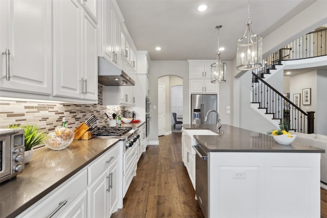 kitchen with white cabinetry, an island with sink, decorative backsplash, pendant lighting, and appliances with stainless steel finishes