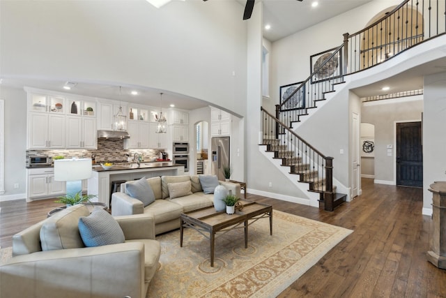 living room with a towering ceiling, dark hardwood / wood-style flooring, and ceiling fan