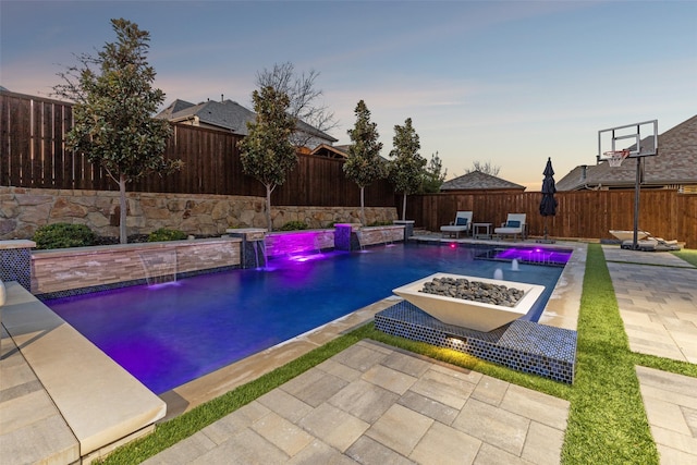 pool at dusk featuring a patio, pool water feature, and an outdoor fire pit