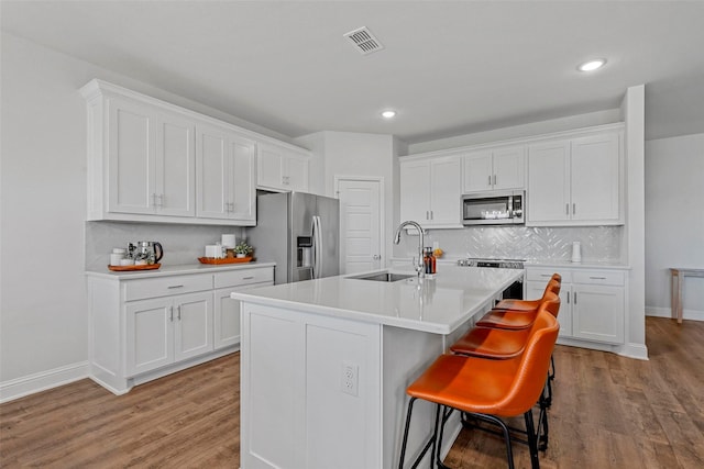 kitchen with sink, white cabinetry, an island with sink, a breakfast bar, and appliances with stainless steel finishes