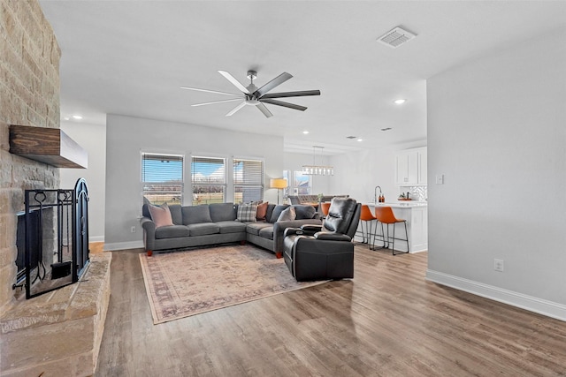 living room featuring ceiling fan, light hardwood / wood-style flooring, and a stone fireplace