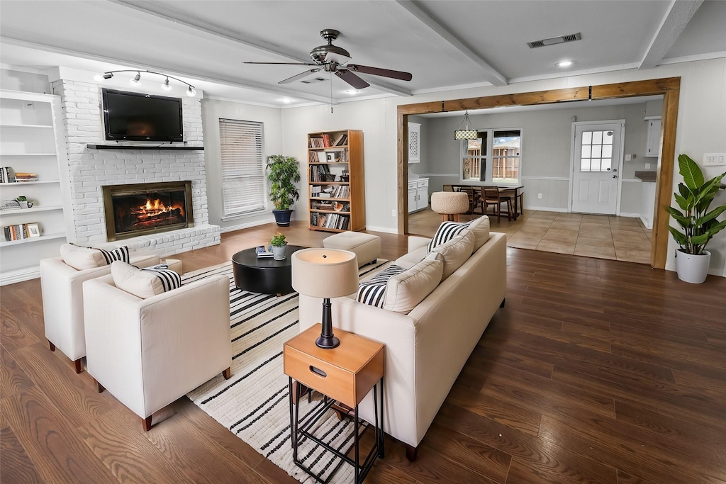 living room with wood-type flooring, crown molding, ceiling fan, a fireplace, and beam ceiling