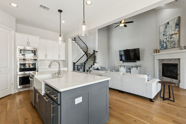 kitchen with white cabinets, ceiling fan, an island with sink, hanging light fixtures, and appliances with stainless steel finishes