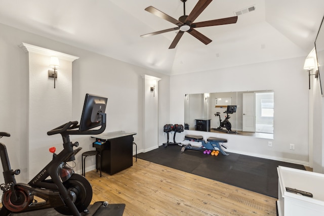 workout area with ceiling fan, light wood-type flooring, vaulted ceiling, and a tray ceiling