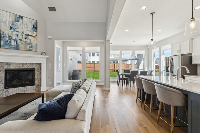 living room with sink, a fireplace, an inviting chandelier, light hardwood / wood-style flooring, and high vaulted ceiling