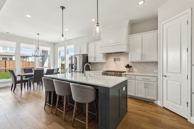 kitchen with stainless steel fridge with ice dispenser, white cabinetry, an island with sink, and premium range hood