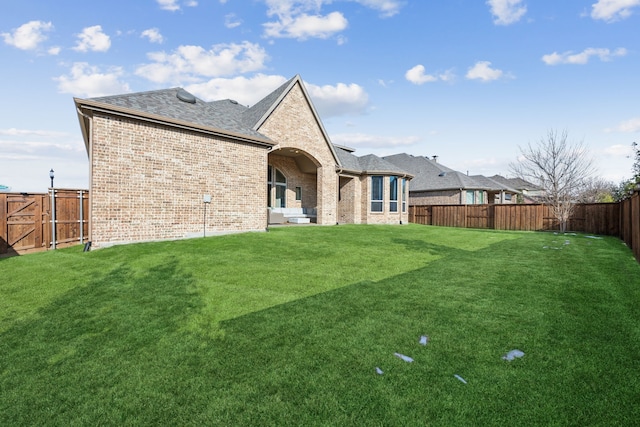 rear view of property featuring a yard, a fenced backyard, a shingled roof, and brick siding