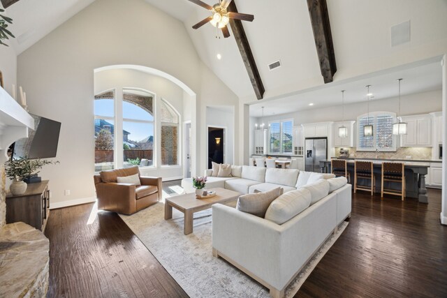 living room with ceiling fan with notable chandelier, a wealth of natural light, a fireplace, and beamed ceiling