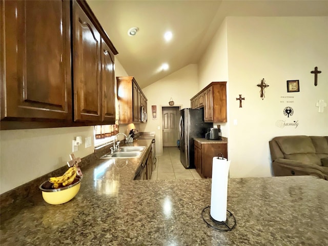 kitchen featuring light tile patterned flooring, dark brown cabinetry, lofted ceiling, sink, and stainless steel refrigerator