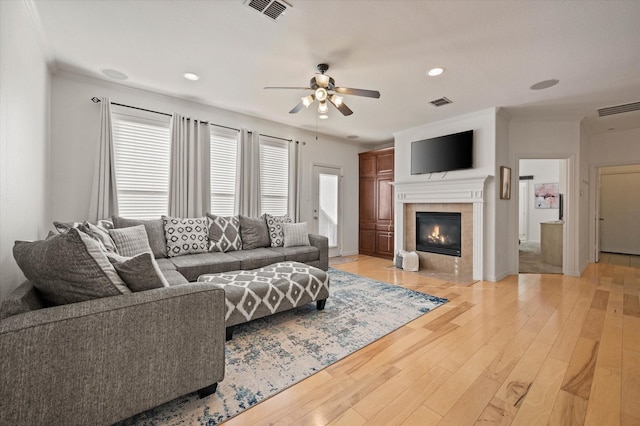 living room featuring ceiling fan, wood-type flooring, a tile fireplace, and crown molding