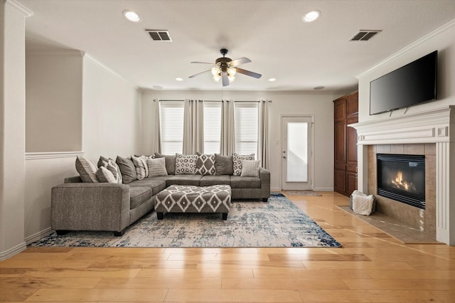 living room featuring ceiling fan, a fireplace, ornamental molding, and light hardwood / wood-style floors