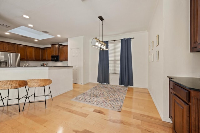 kitchen featuring stainless steel fridge with ice dispenser, a skylight, decorative backsplash, light wood-type flooring, and hanging light fixtures