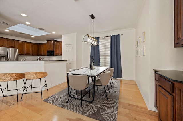 dining space featuring a skylight, light hardwood / wood-style floors, a chandelier, and ornamental molding