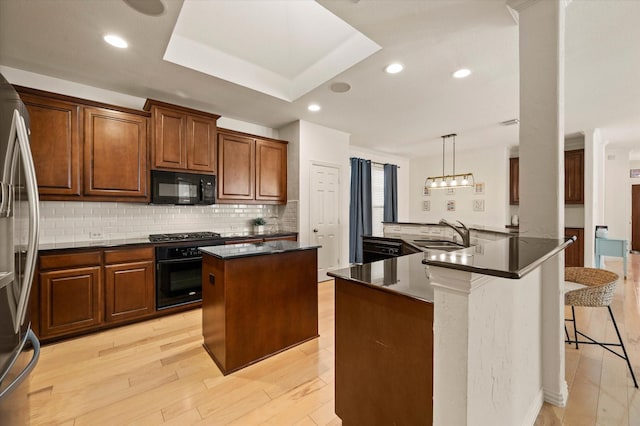 kitchen featuring decorative light fixtures, a center island, black appliances, decorative backsplash, and sink