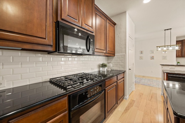 kitchen featuring backsplash, light wood-type flooring, dark stone countertops, pendant lighting, and black appliances