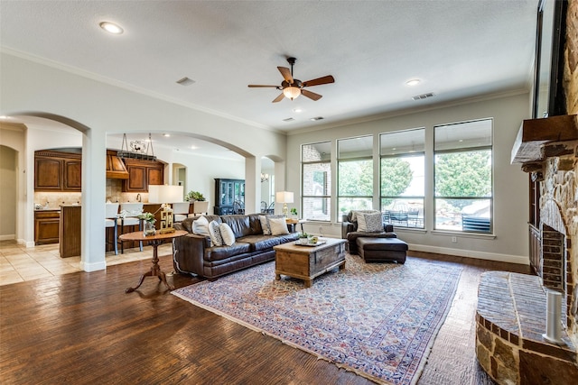 living room featuring a ceiling fan, a fireplace with raised hearth, arched walkways, light wood finished floors, and visible vents