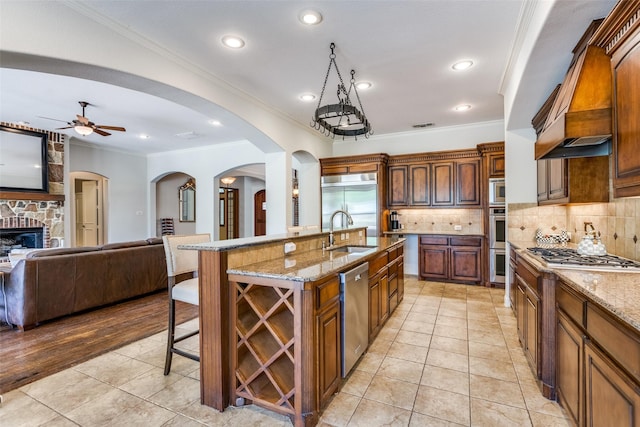 kitchen featuring ceiling fan, a spacious island, a kitchen bar, sink, and a stone fireplace