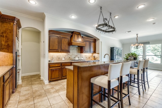 kitchen with light stone countertops, pendant lighting, a kitchen island with sink, and an inviting chandelier